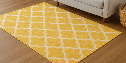 A yellow Moroccan trellis area rug on a wooden floor beside a light gray sofa and a woven basket with a throw blanket.