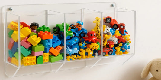 A clear wall-mounted toy dispenser filled with colorful blocks, cars, and animal figures, organized in three separate transparent sections.