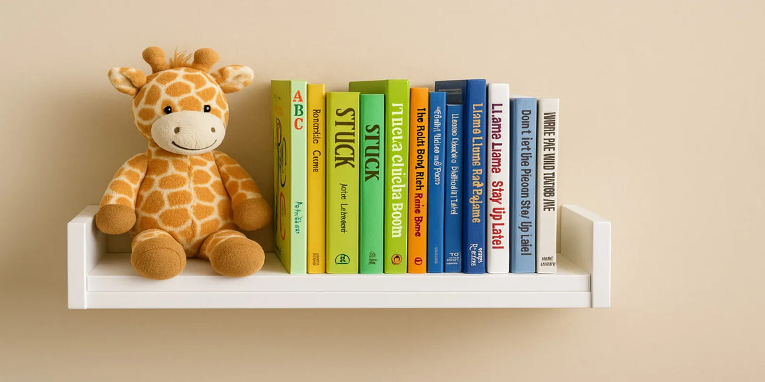 A white floating bookshelf on a beige wall holds a plush giraffe toy and colorful children's books arranged neatly in warm, soft lighting