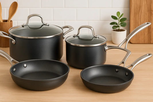 A modern nonstick cookware set with pots and pans featuring stainless steel handles and glass lids, displayed on a wooden kitchen counter.